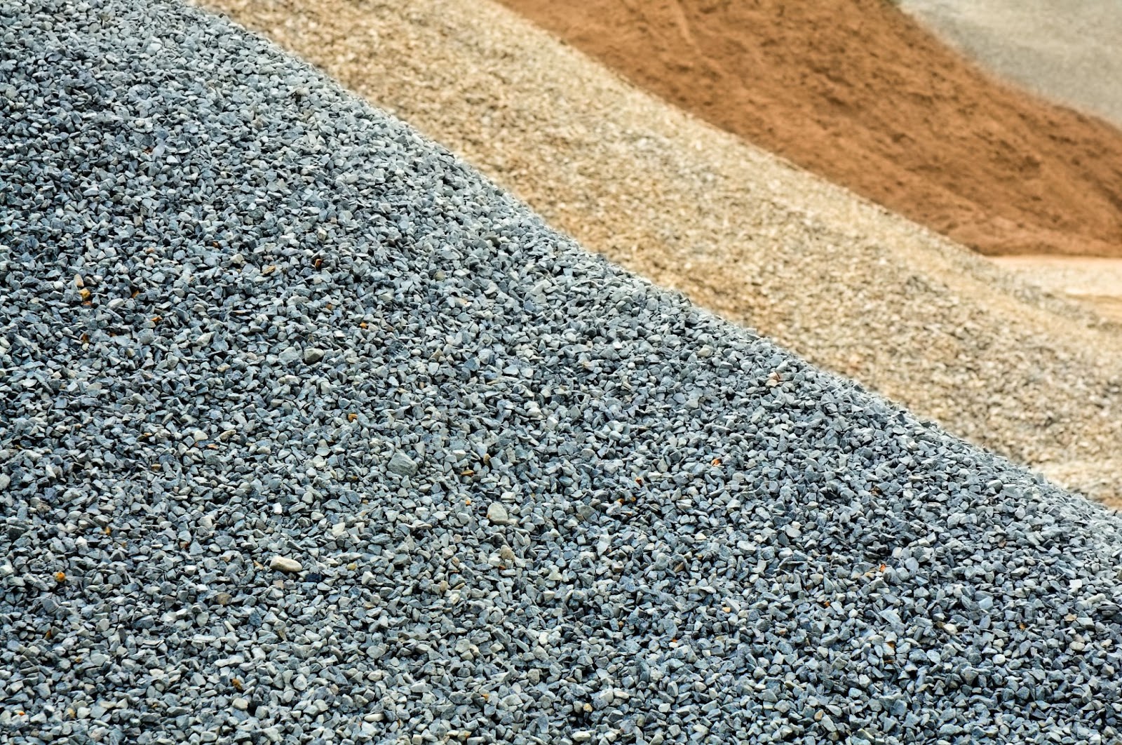 Piles of construction raw materials including gravel, grit and sand.